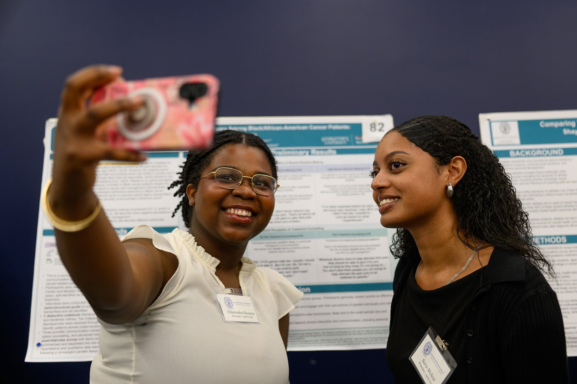 Two students take a selfie in front of their posters