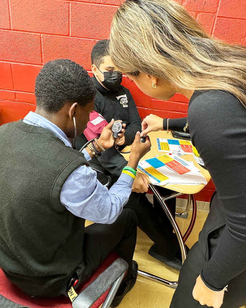 A Georgetown student teaches a high school student how to take a blood pressure reading