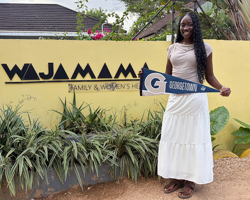 Kayla Wontumi holds a Georgetown pennant and stands before a yellow sign that says WAJAMAMA in black letters