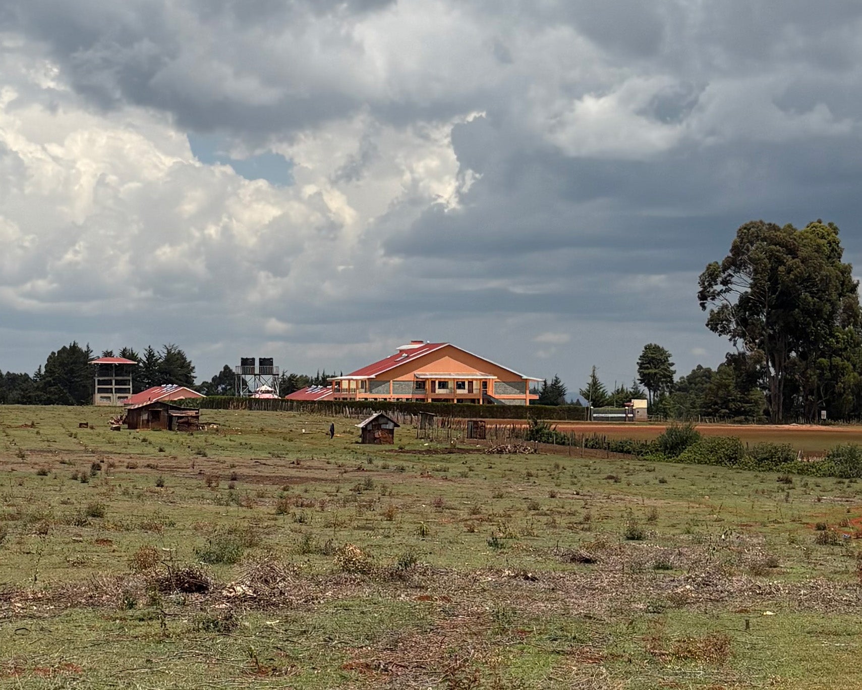 A building with red tile roof surrounded by smaller outbuildings in a flat meadow area